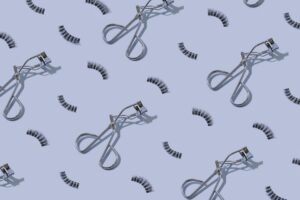eyelashes and eye lash curlers perfectly laid out as a collage against a blue background